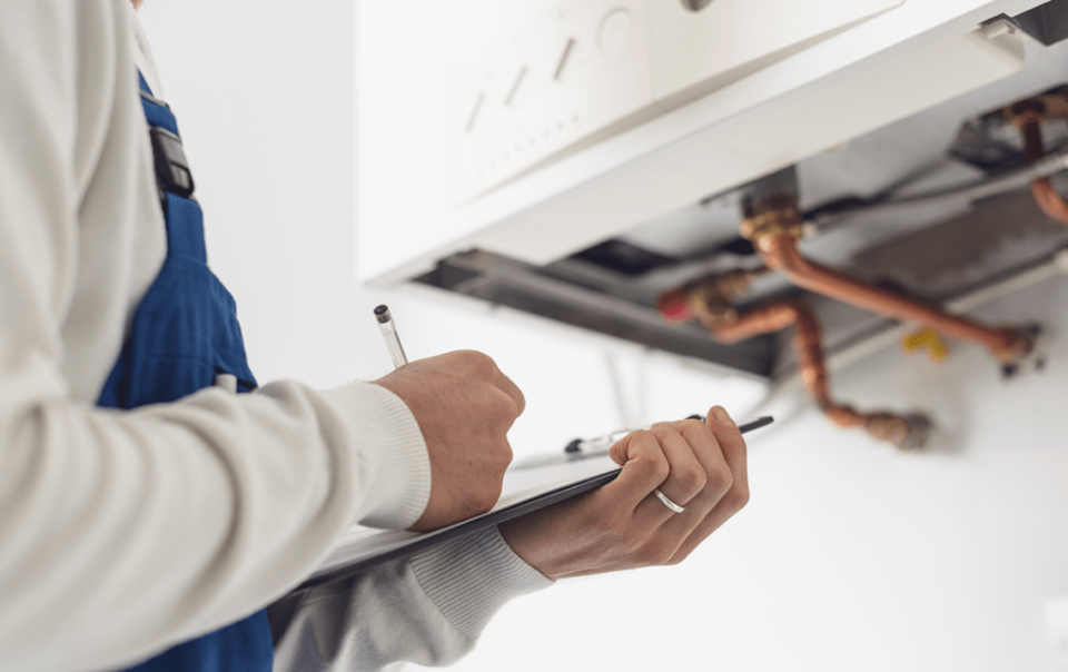 Técnico realizando uma inspecção técnica num sistema de aquecimento de imóvel, verificando as tubagens e registando as suas observações num impresso.