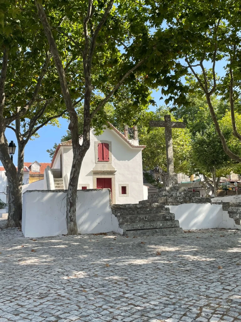 "Largo da capela tradicional e cruzeiro de pedra na aldeia do Livramento, ilustrando a paz e autenticidade da zona de Alcabideche.