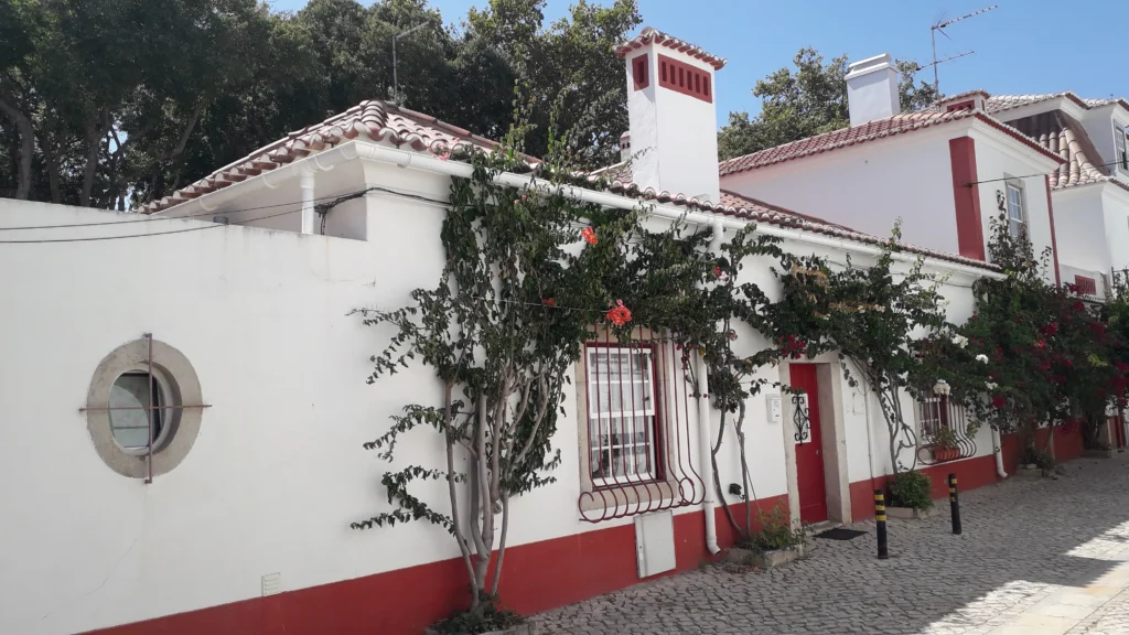 Fachada de moradia tradicional com traça portuguesa e buganvílias numa rua de calçada no Centro Histórico de Cascais.
